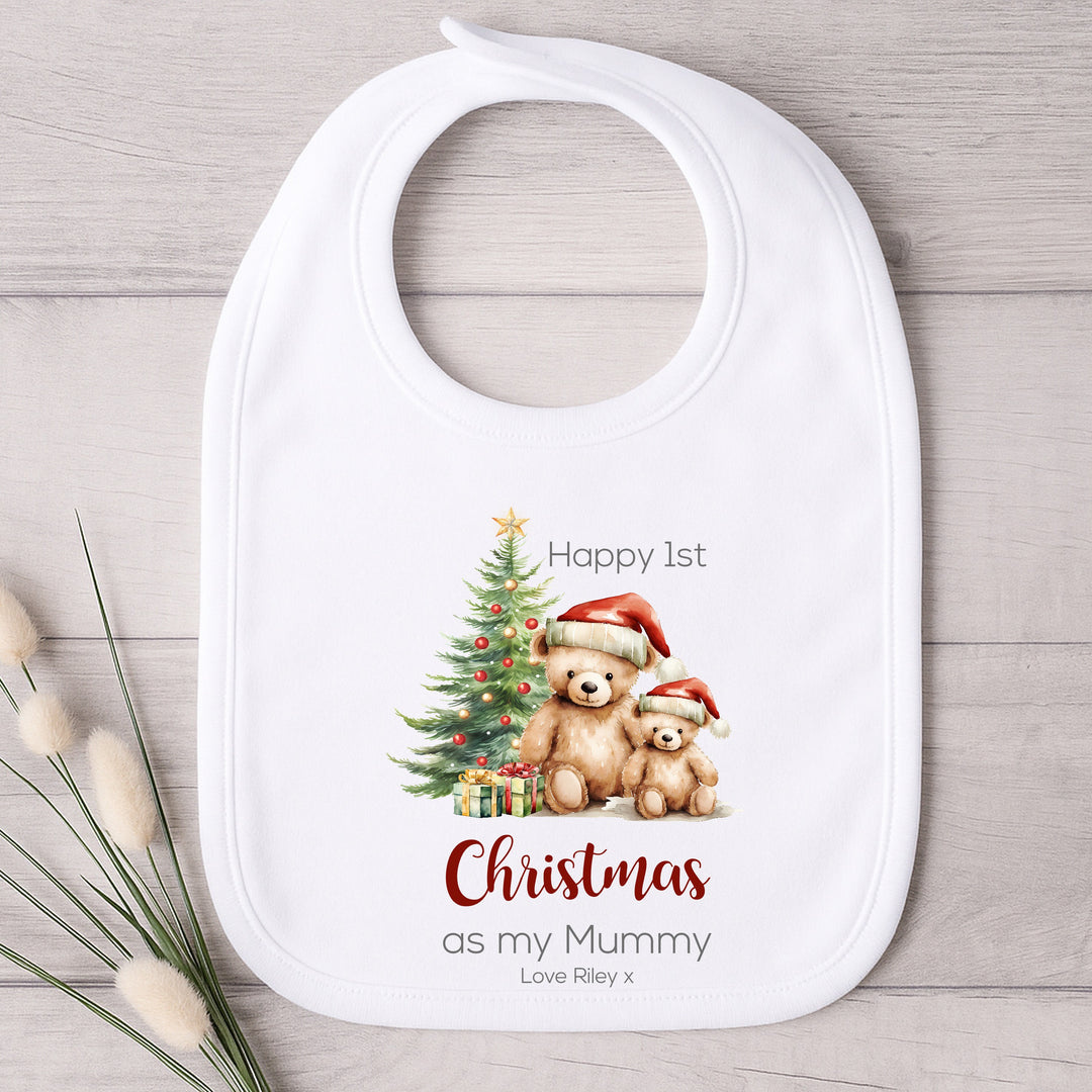 White bib with Christmas-themed design of two bears and a tree, on a wooden surface.