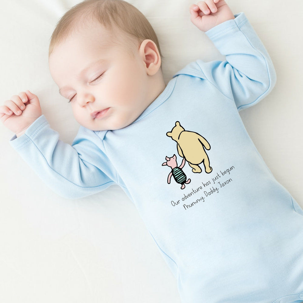 a personalised blue baby grow that says 'Our adventure has jusy begun Mummy, Daddy, Jaxon'. This design features a classic winnie the pooh and piglet