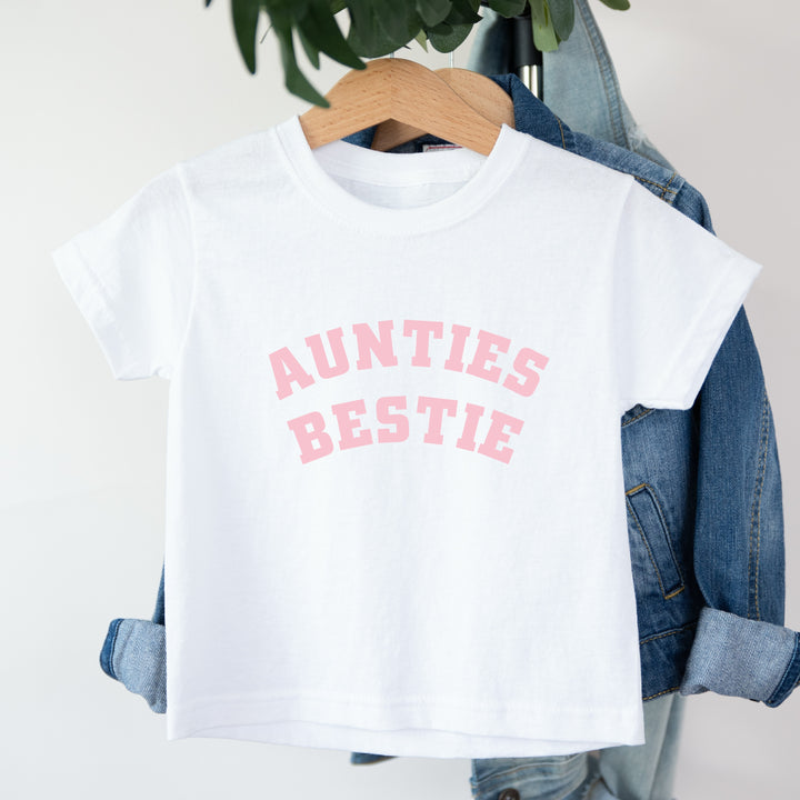 White t-shirt with 'AUNTIES BESTIE' text on a hanger with denim jacket.
