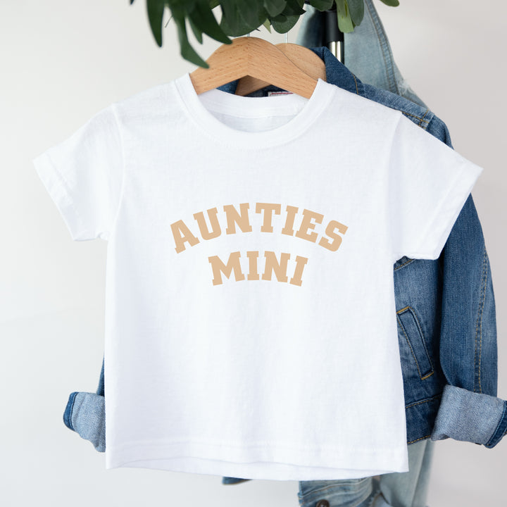 White t-shirt with 'AUNTIES MINI' text on a hanger with denim jacket.