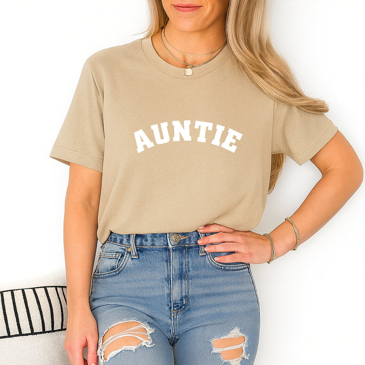 Person wearing a beige t-shirt with 'AUNTIE' text and ripped jeans on a white background