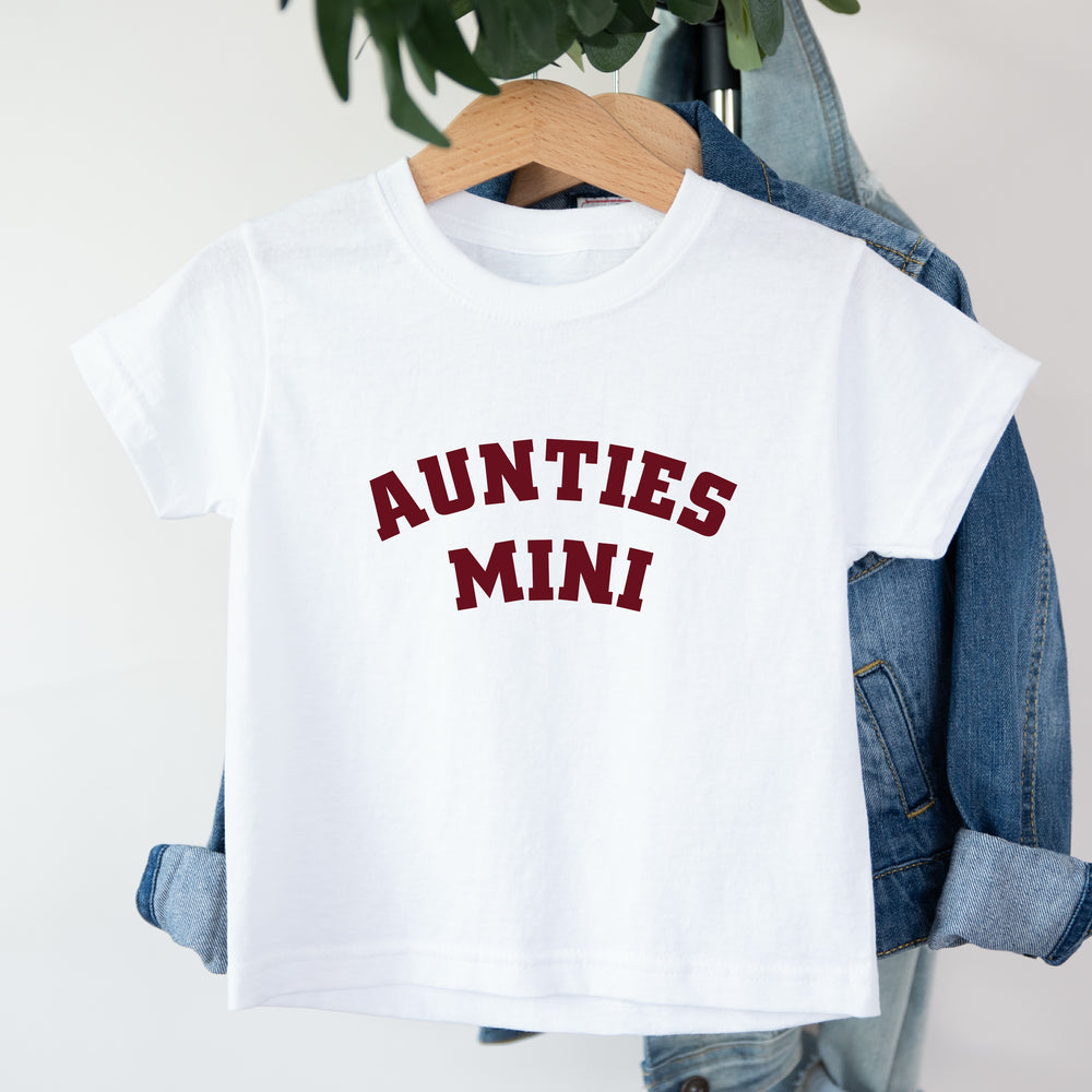 White t-shirt with 'AUNTIES MINI' text on a hanger with denim jacket.