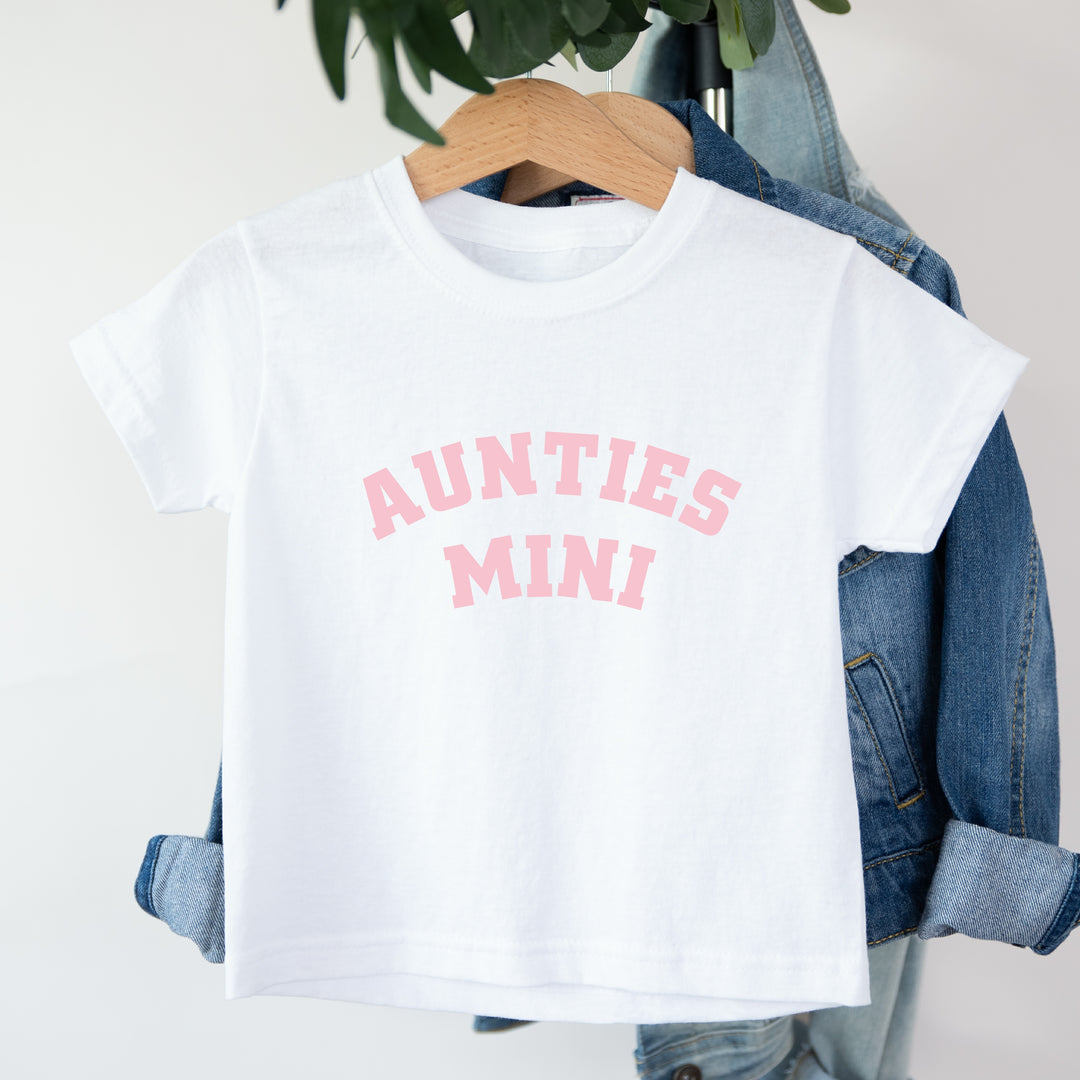 White t-shirt with 'AUNTIES MINI' text on a hanger with denim jacket.