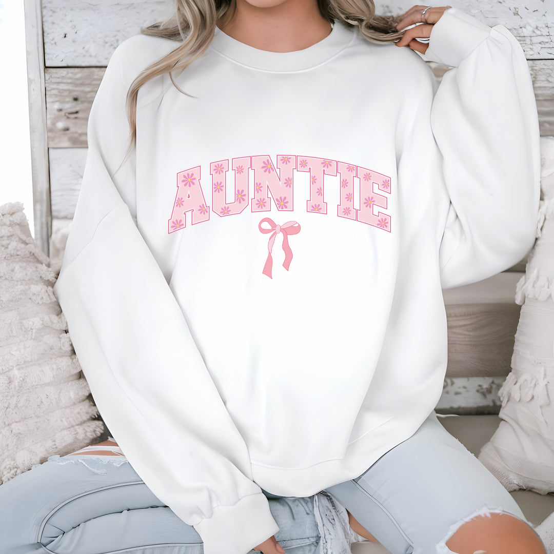 White sweatshirt with pink 'Auntie' text and bow graphic worn by a person.