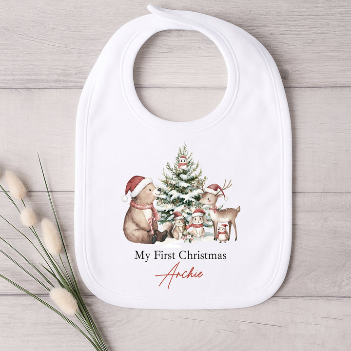 Baby bib with Christmas design and 'My First Christmas Archie' text on a wooden surface.
