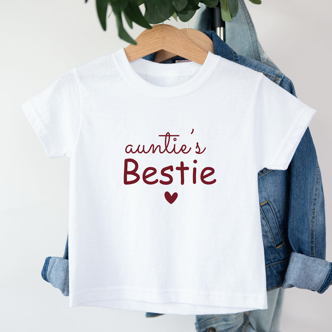 White t-shirt with 'auntie's Bestie' text and heart on a hanger with denim jacket.