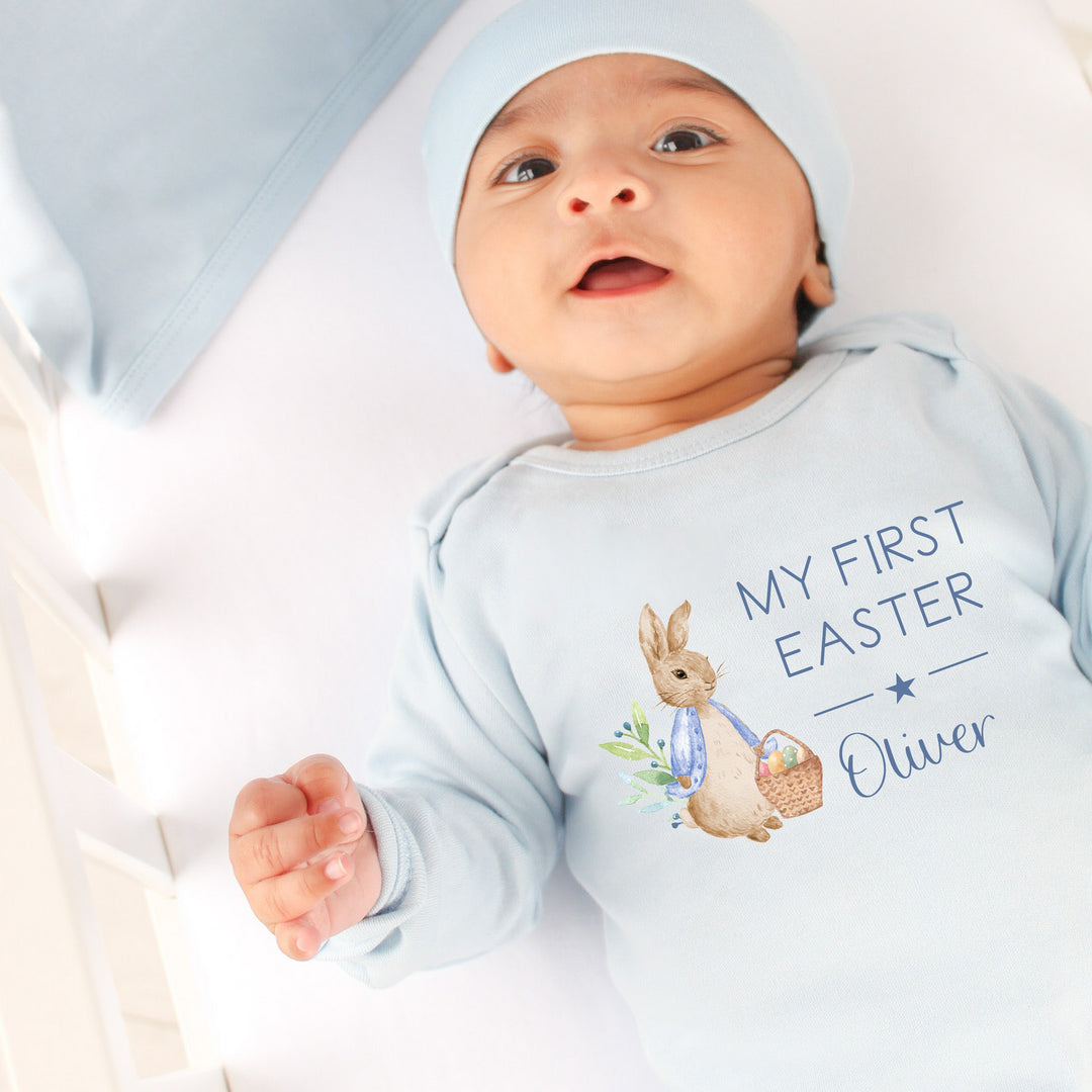 Personalised blue Easter babygrow that says 'My First Easter Oliver'. This design features a rabbit wearing a blue jacket holding an Easter basket