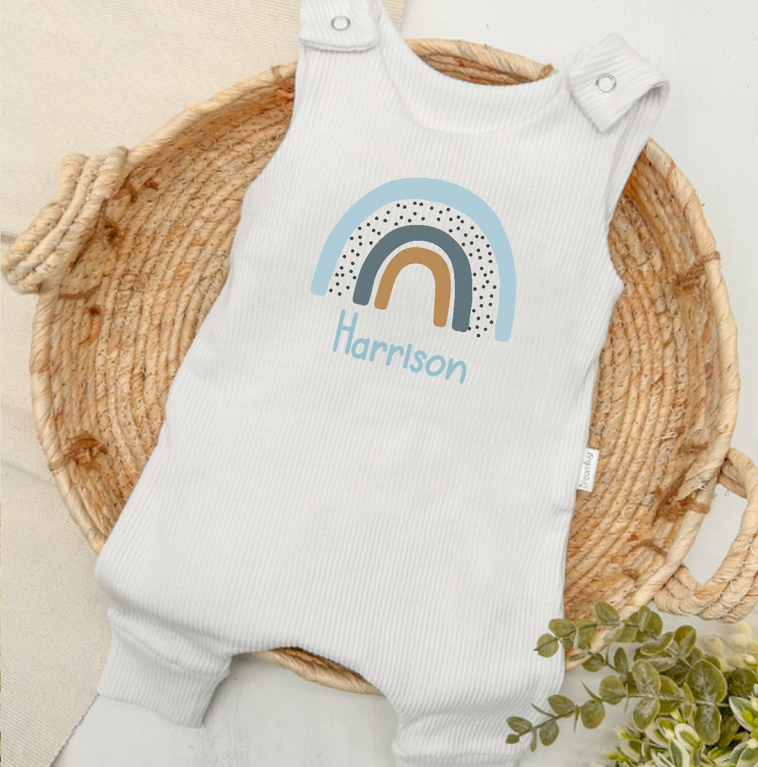 Personalised white ribbed dungarees that say 'Harrison'. This design features a blue rainbow
