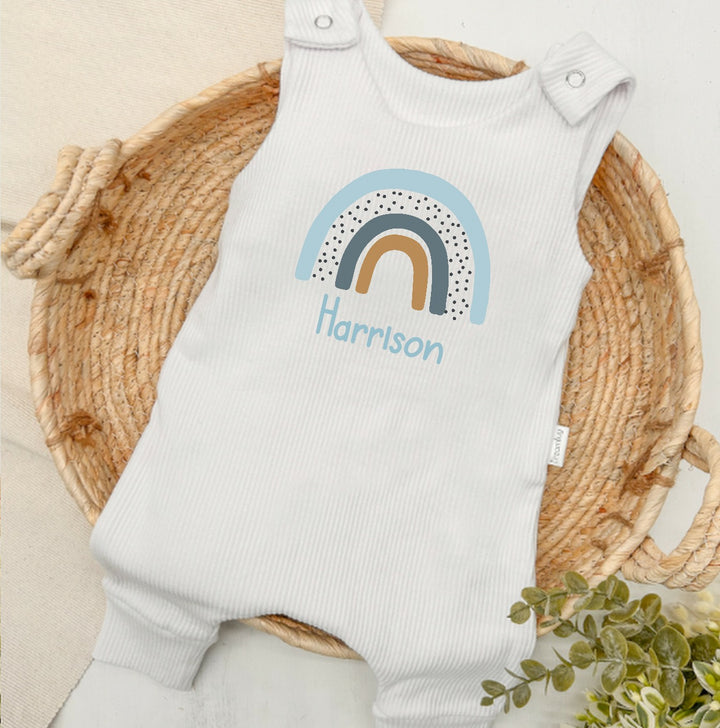 Personalised white ribbed dungarees that say 'Harrison'. This design features a blue rainbow