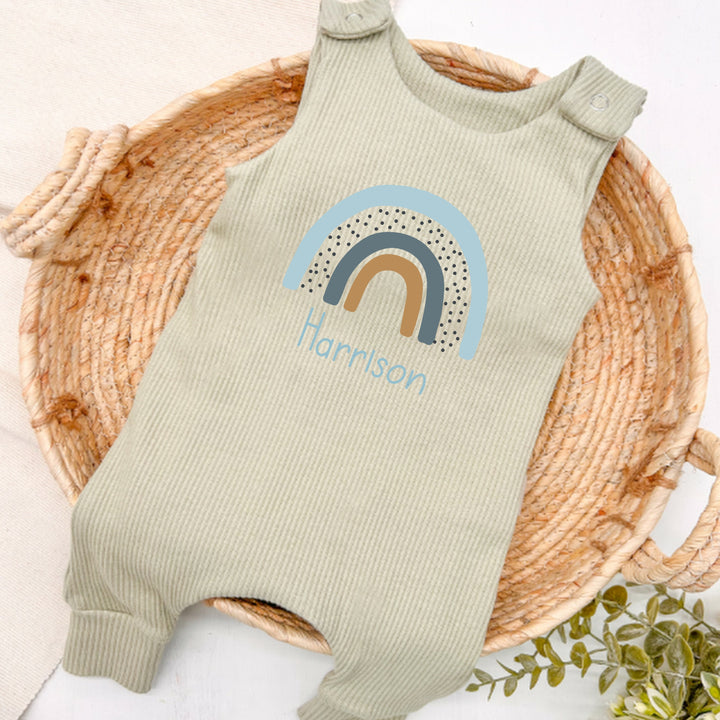 Personalised sage green ribbed dungarees that say 'Harrison'. This design features a blue rainbow