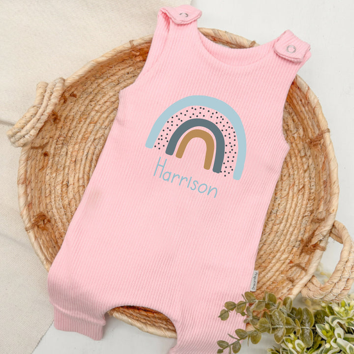 Personalised pink ribbed dungarees that say 'Harrison'. This design features a blue rainbow