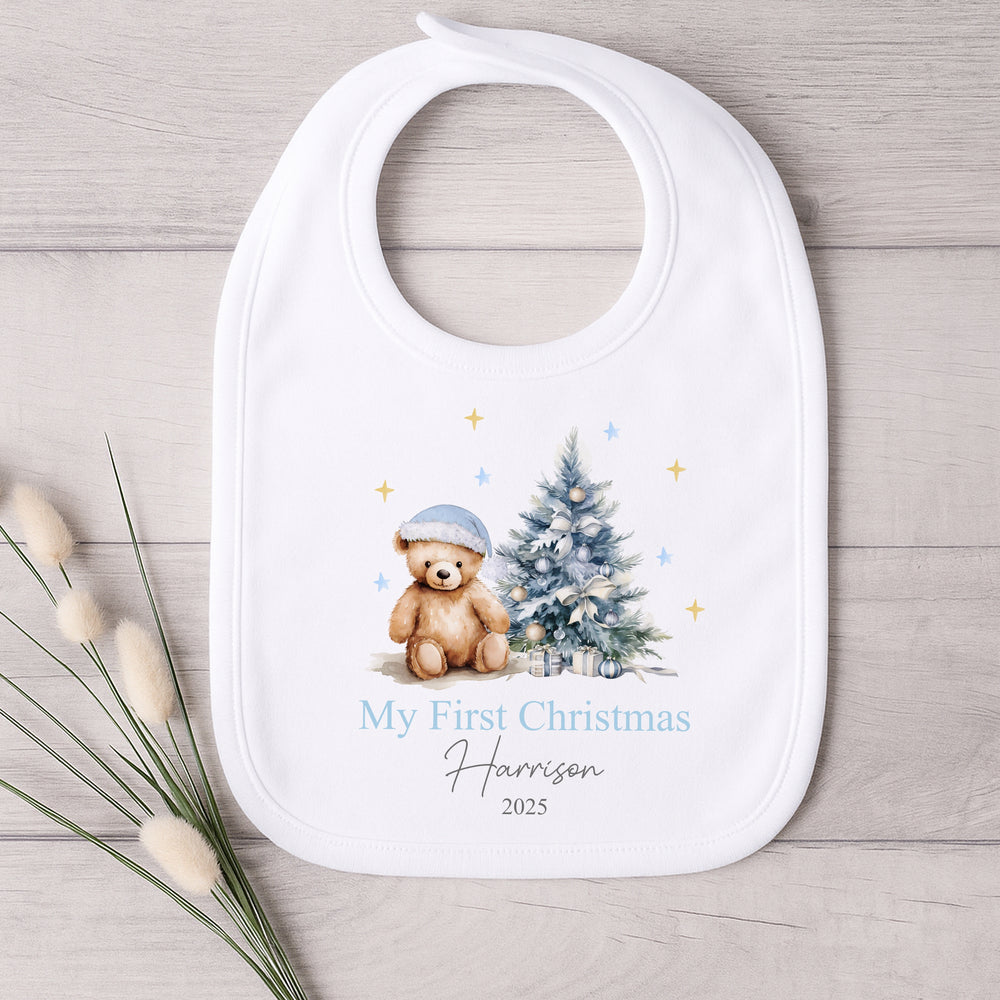 Baby bib with Christmas design featuring a teddy bear and tree, on a wooden surface.