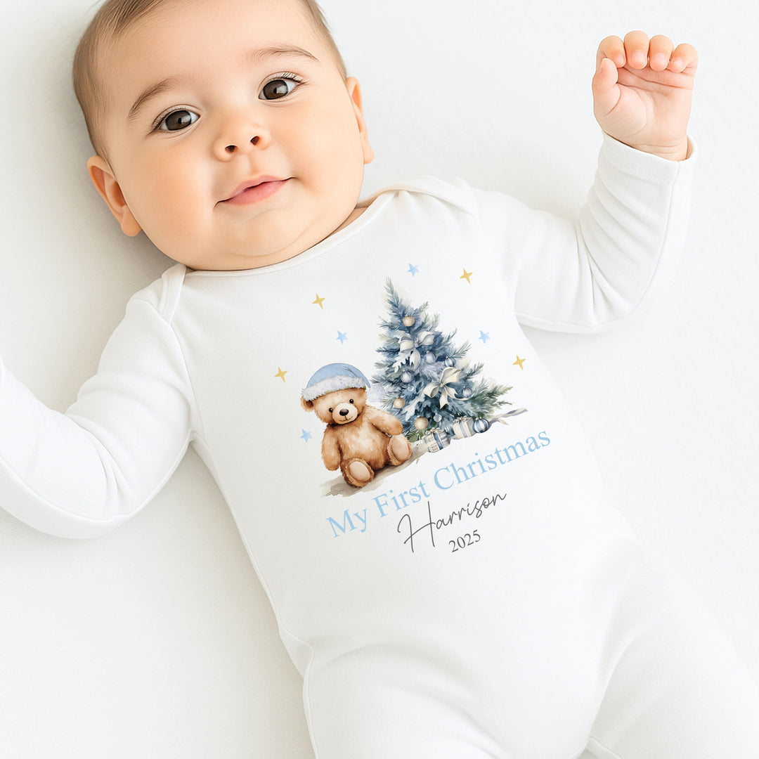 Baby wearing a white onesie with a Christmas design and text, sitting on a white surface.