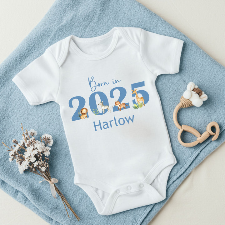 a personalised white baby vest that says 'Born in 20245 Harlow'. This design features safari animals