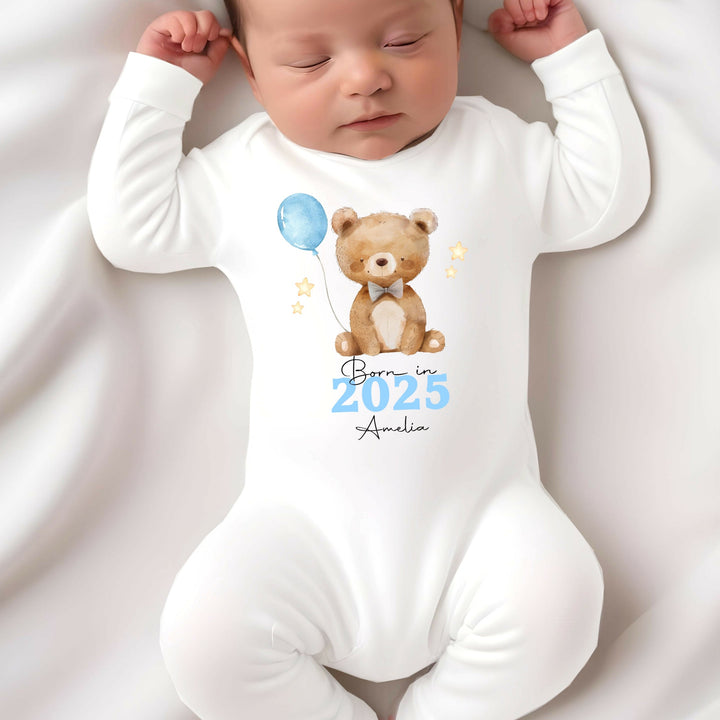 a personalised white baby grow that says 'Born in 2025 Amelia'. This design features a brown teddy holding a blue balloon