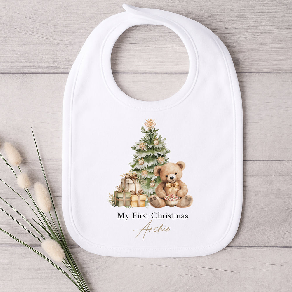 Baby bib with Christmas design featuring a teddy bear and tree, on a wooden surface.