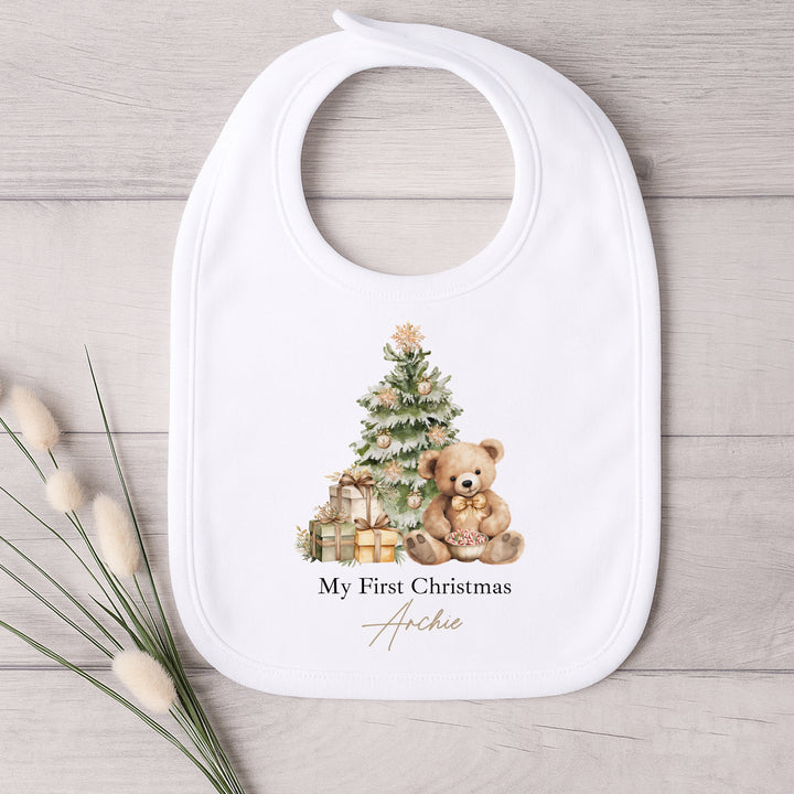 Baby bib with Christmas design featuring a teddy bear and tree, on a wooden surface.