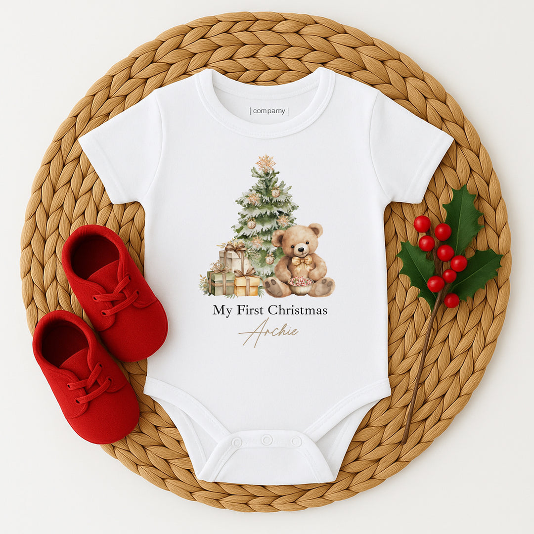 White baby onesie with Christmas design and red shoes on a woven mat