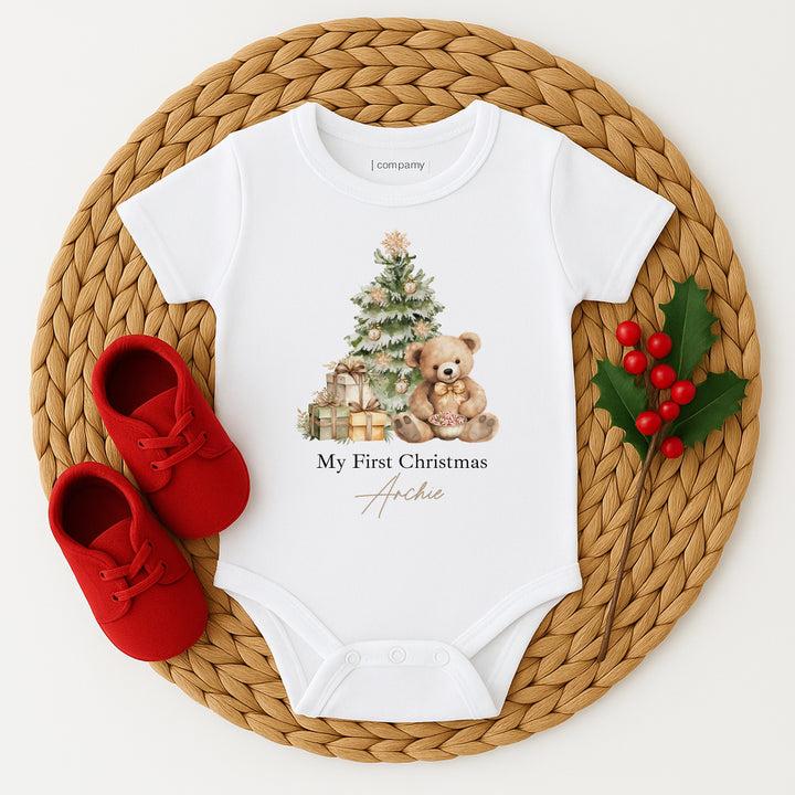 White baby onesie with Christmas design and red shoes on a woven mat