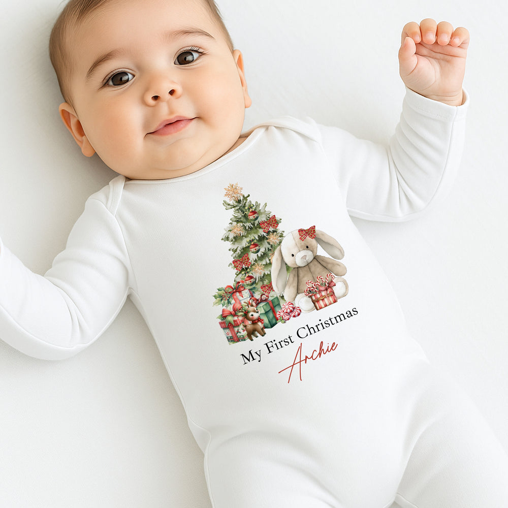 Baby wearing a white onesie with a Christmas design and text, lying on a white surface.