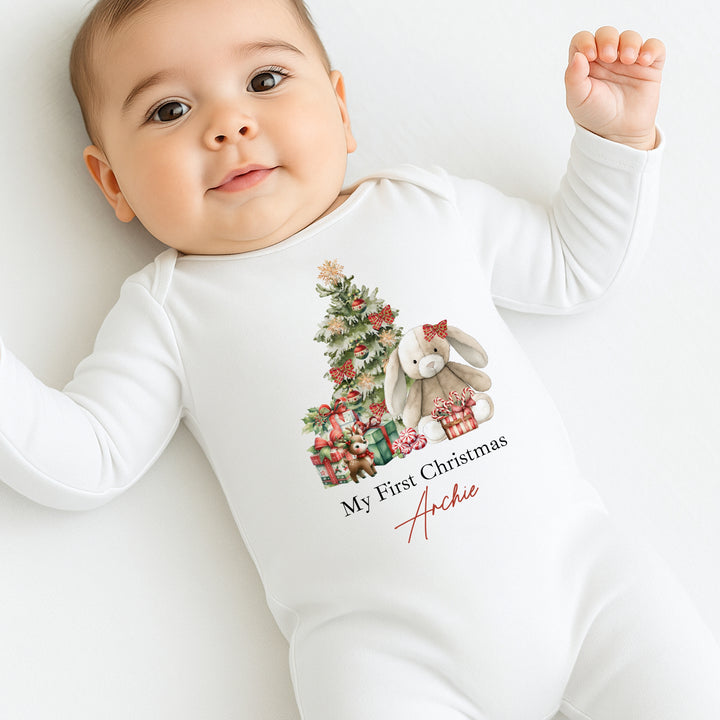 Baby wearing a white onesie with a Christmas design and text, lying on a white surface.