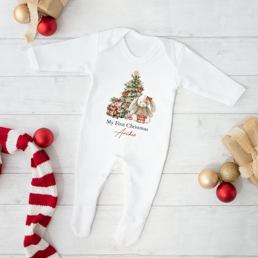 White baby onesie with Christmas design and text, surrounded by festive decorations on a light wooden surface.
