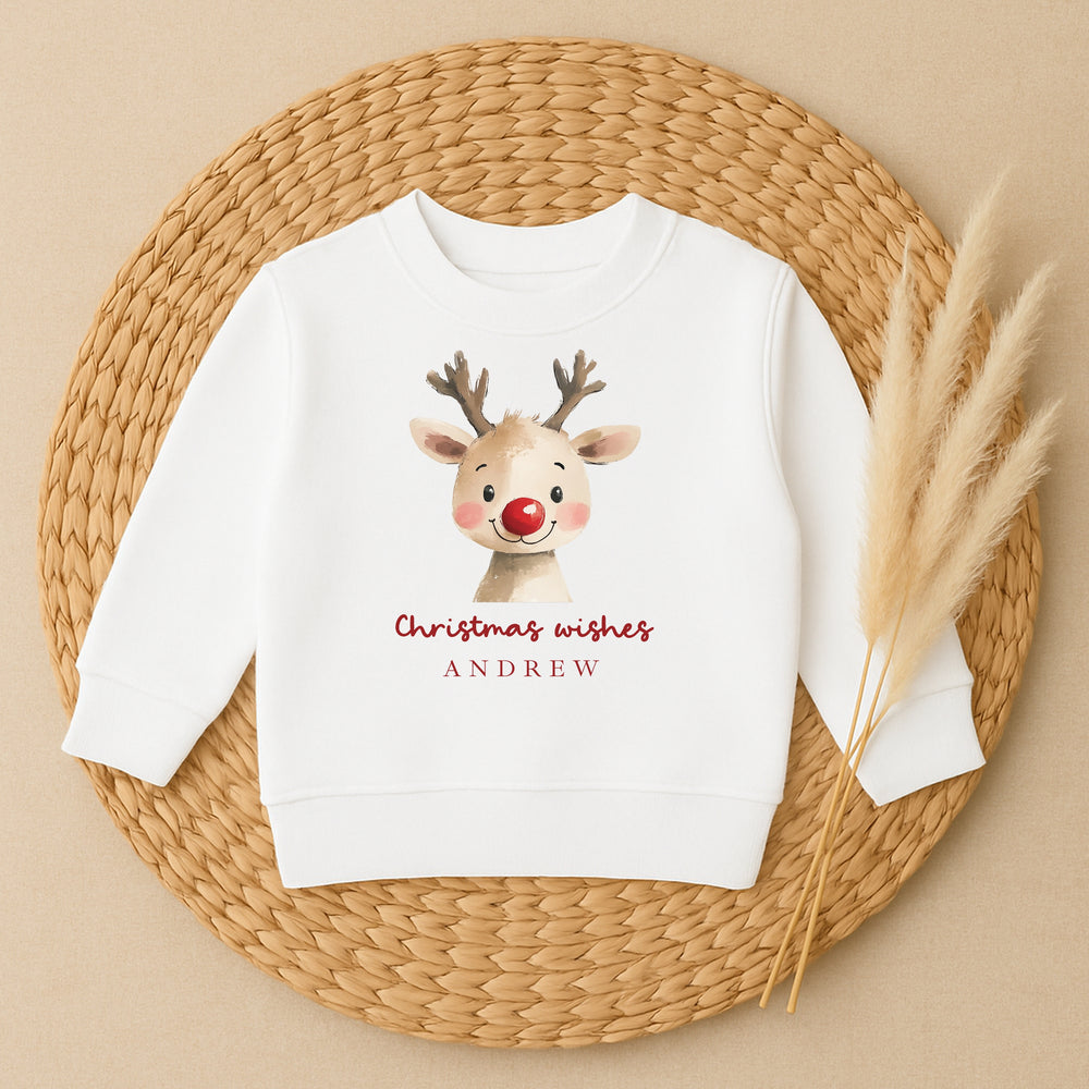 White sweatshirt with a reindeer design and 'Christmas wishes ANDREW' text on a woven mat.