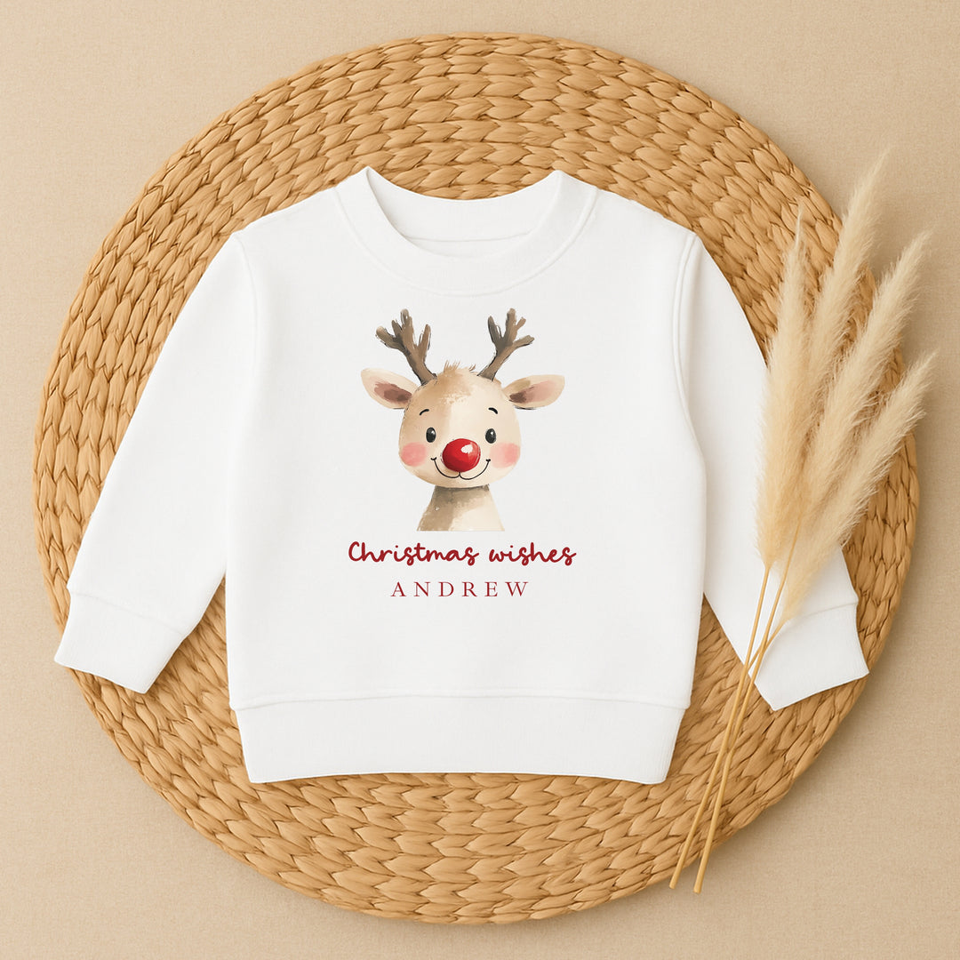 White sweatshirt with a reindeer design and 'Christmas wishes ANDREW' text on a woven mat.