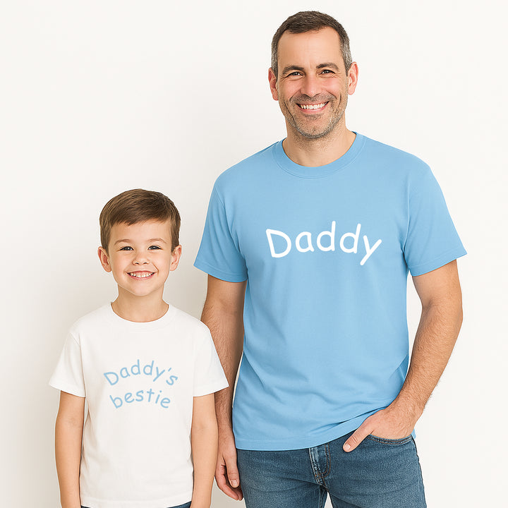 Man and child wearing matching 'Daddy' and 'Daddy's bestie' shirts on a plain background