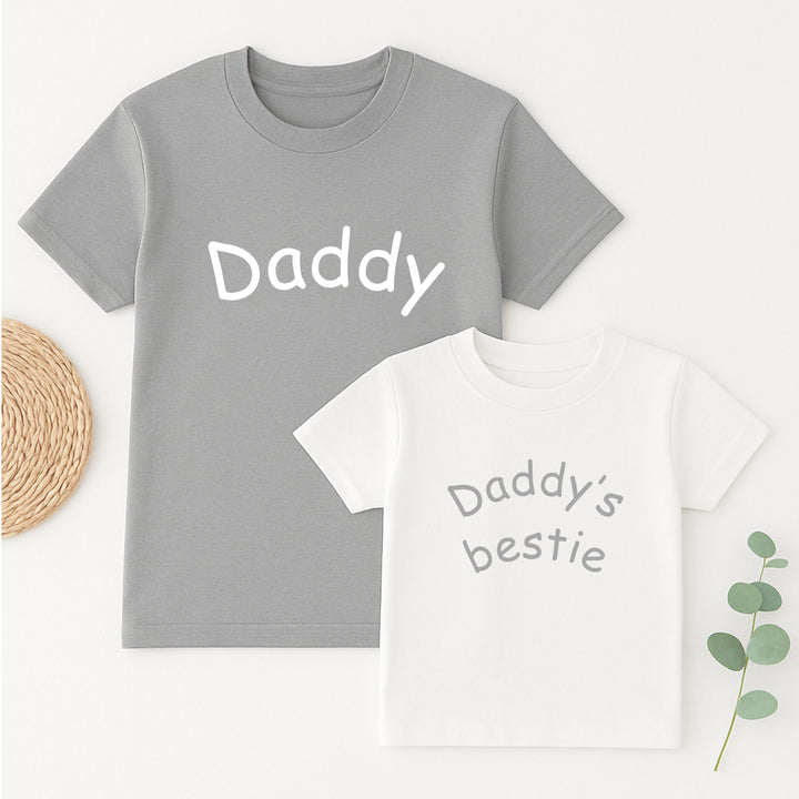 Gray t-shirt with 'Daddy' and white t-shirt with 'Daddy's bestie' on a light background