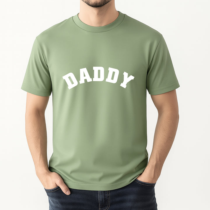 Person wearing a green t-shirt with 'DADDY' printed on it against a white background