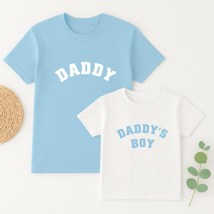 Light blue t-shirt with 'DADDY' and white t-shirt with 'DADDY'S BOY' text on a white background.