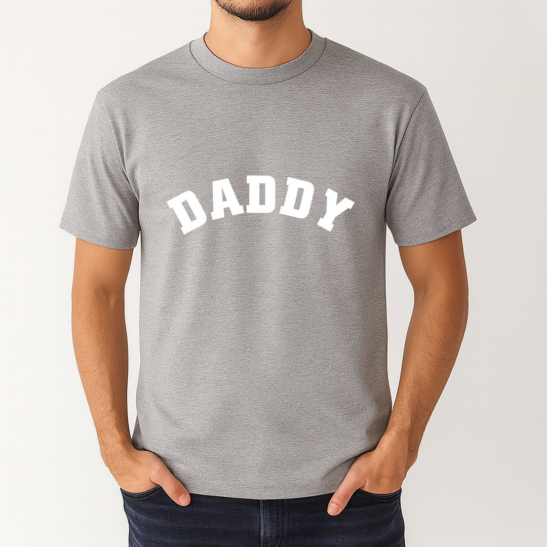 Gray t-shirt with 'DADDY' printed on it worn by a person against a white background