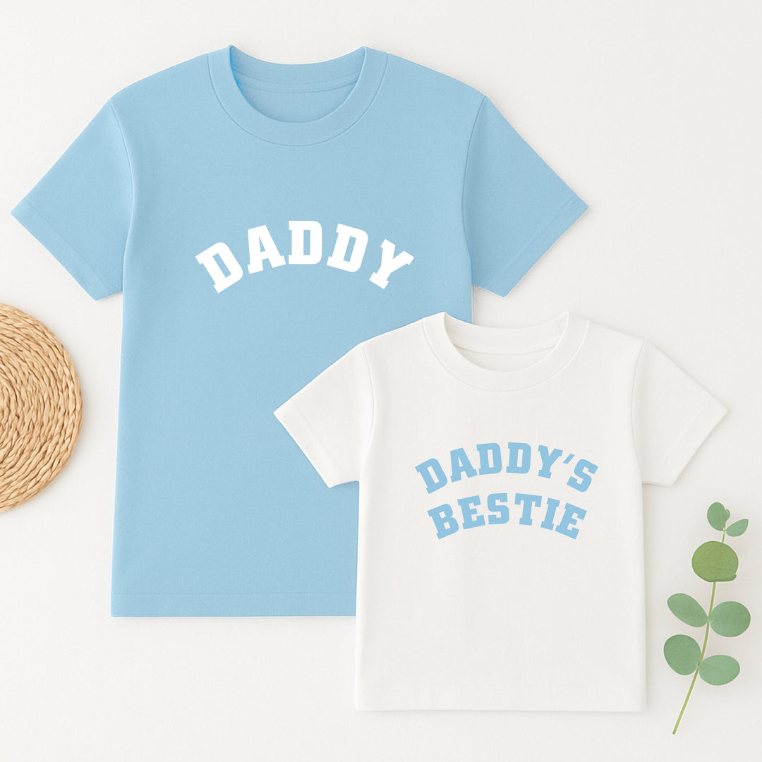 Light blue t-shirt with 'DADDY' text and white t-shirt with 'DADDY'S BESTIE' text on a white background.