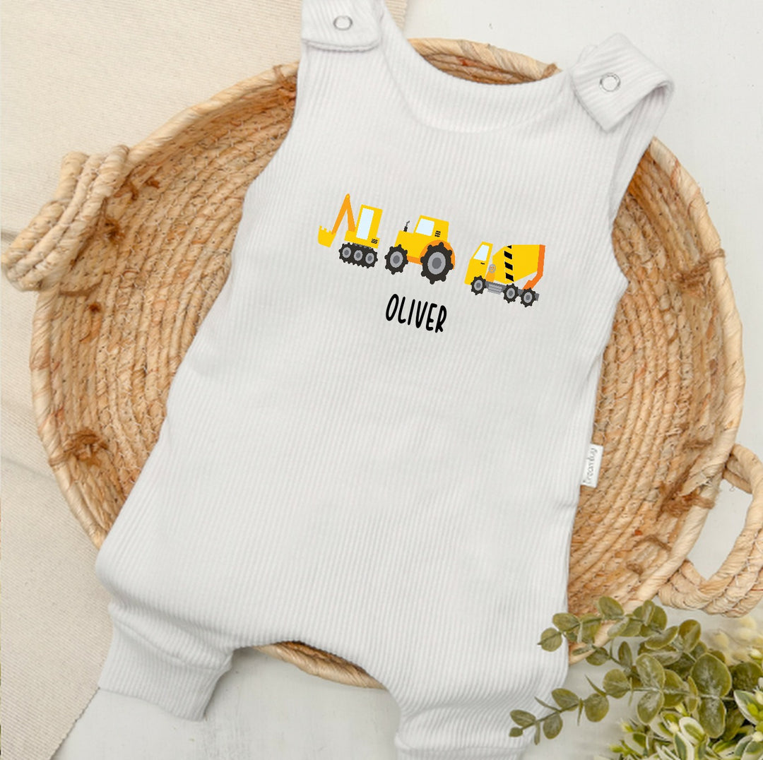 Personalised white ribbed dungarees that say 'Oliver'. This design features 3 diggers