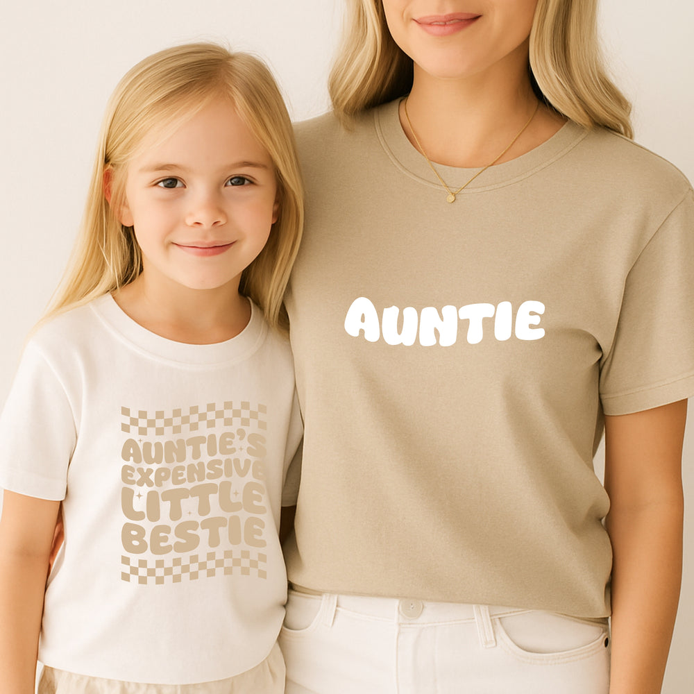Two people wearing matching t-shirts with text, one saying 'Auntie' and the other 'Auntie's Expensive Little Bestie'.