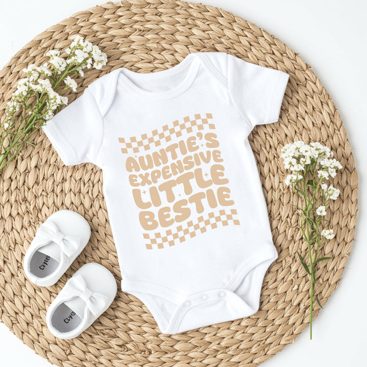 White baby onesie with text and white baby shoes on a woven mat with flowers