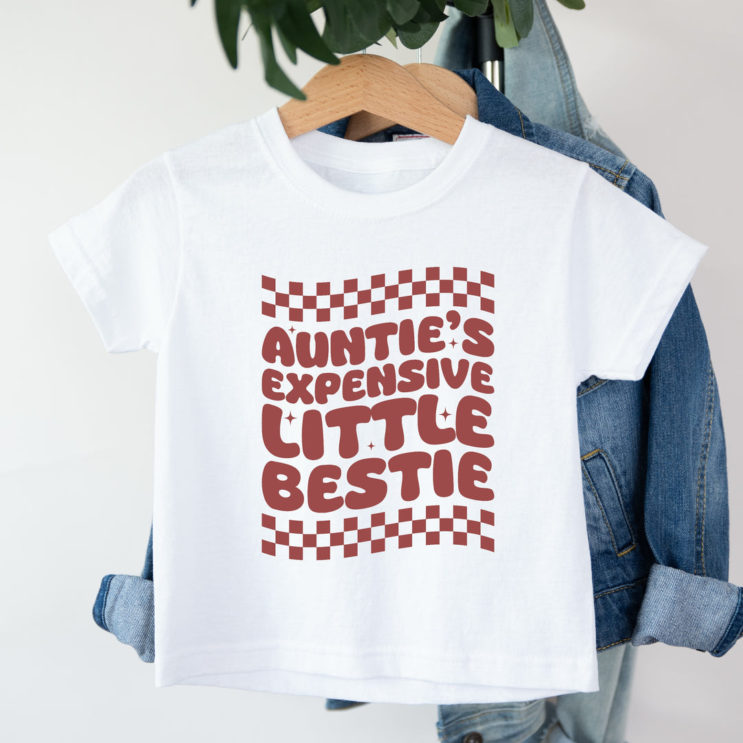 White t-shirt with red text and checkered pattern on a hanger with denim jacket.