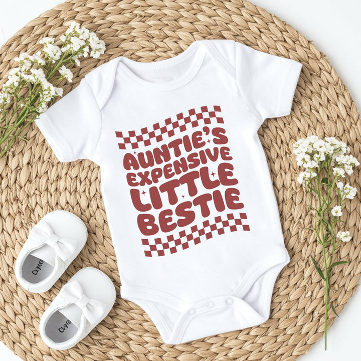 White baby onesie with red text on a woven mat with white flowers