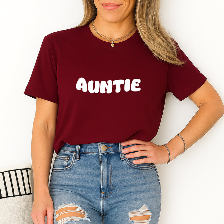 Person wearing a maroon t-shirt with 'AUNTIE' text and ripped jeans on a white background