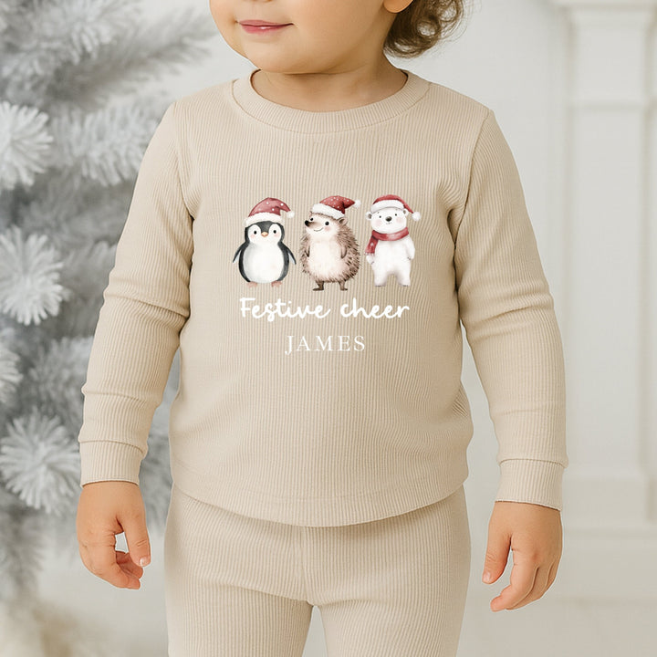 Child wearing a beige outfit with festive designs and text, standing in front of a decorated Christmas tree.