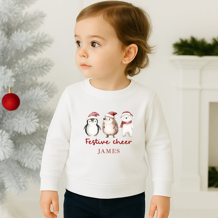 Child wearing a white sweater with Christmas-themed design and text, standing in front of a decorated tree.