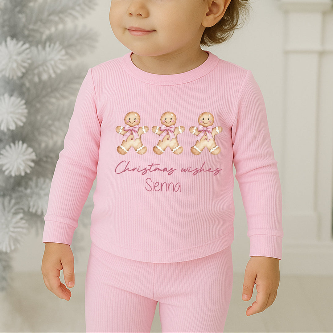 Child wearing pink Christmas-themed pajamas with gingerbread design and text.