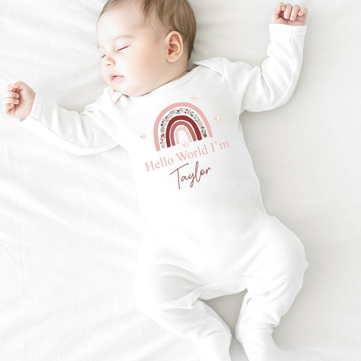 a personalised white baby grow that says 'Hello World I'm Taylor'. This design features a pink floral rainbow