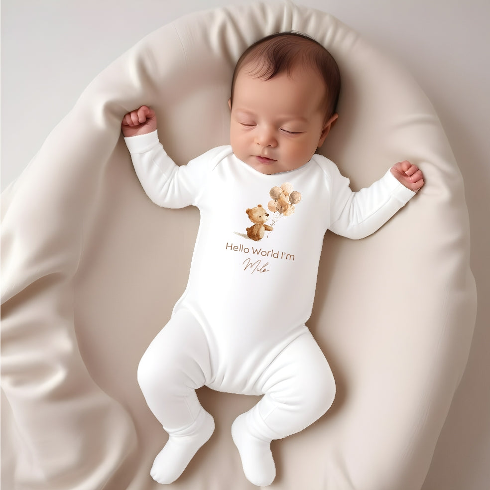 A personalised white baby grow/sleepsuit that says 'Hello World I'm Milo'. This design features a little brown bear holding a bunch of balloons