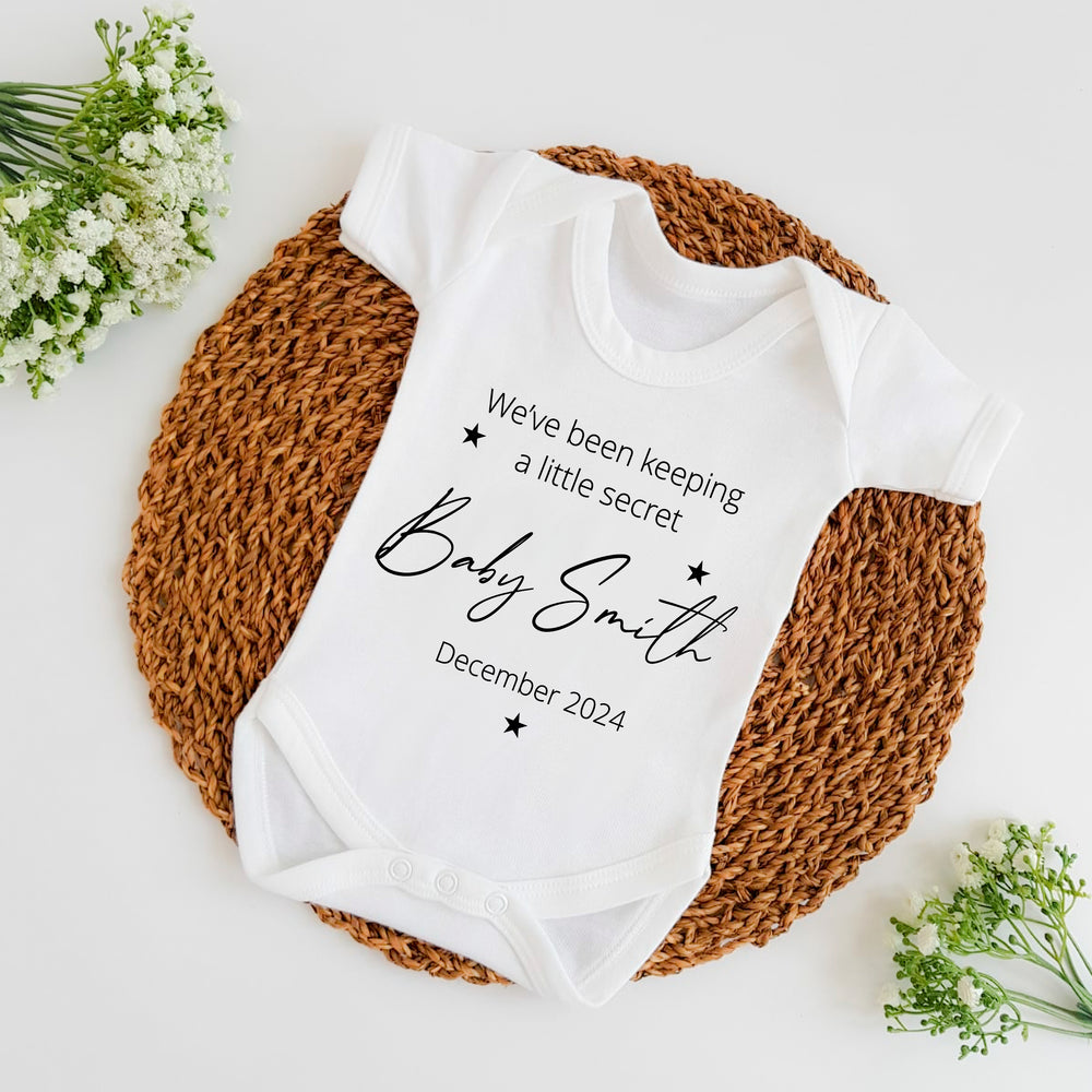 Baby announcement vests that says: We've been keeping a little secret Baby Smith Due December 2024