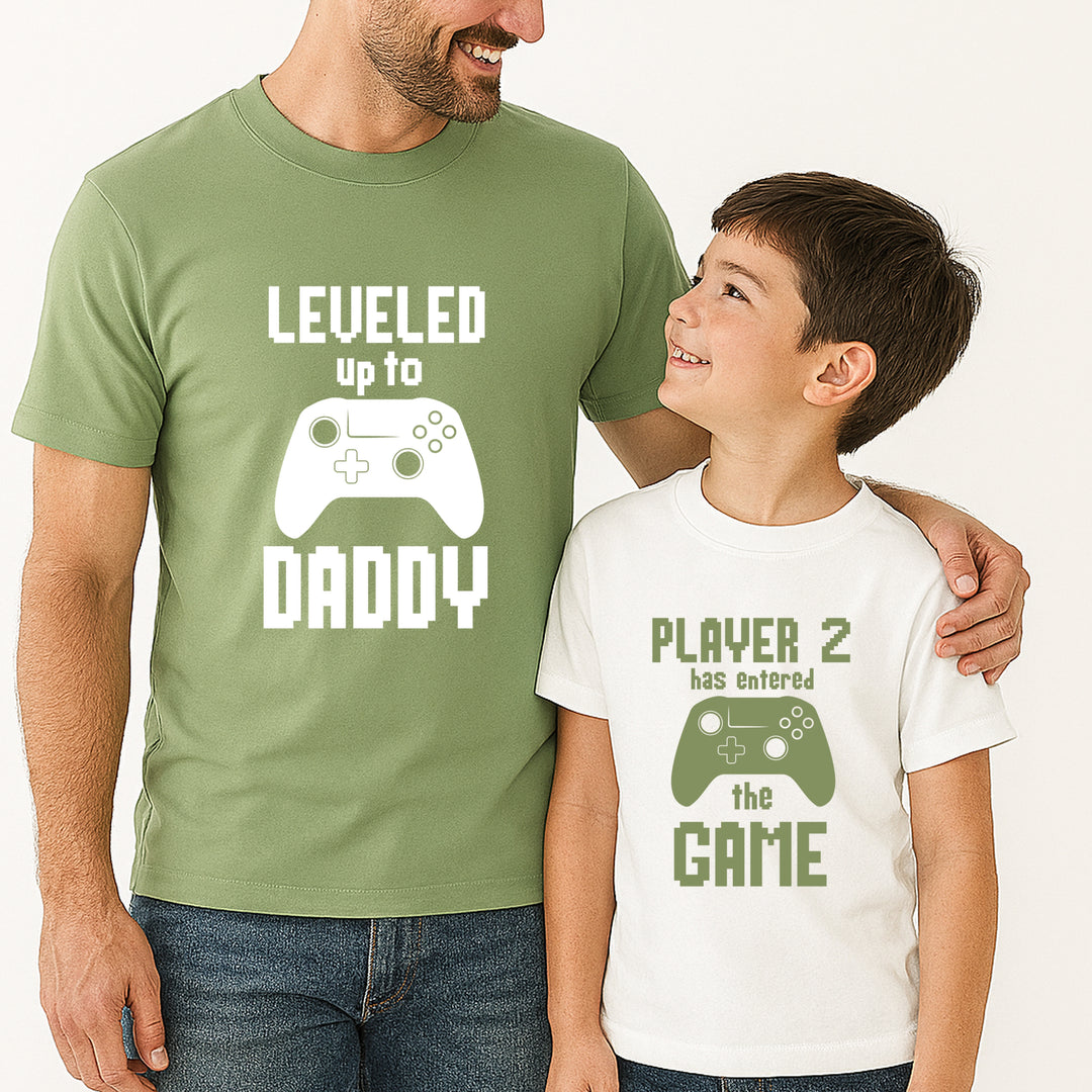Man and child wearing matching green and white t-shirts with gaming-themed text and graphics.
