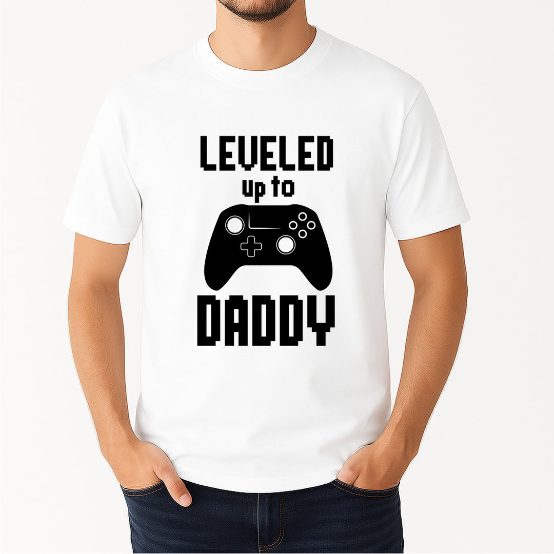 White t-shirt with a graphic of a game controller and text 'Leveled up to Daddy' on a white background.