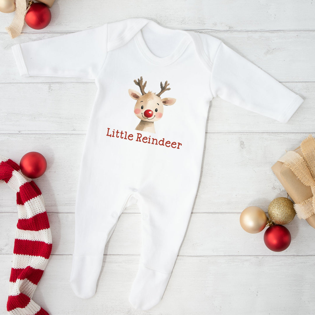 White baby onesie with reindeer design and 'Little Reindeer' text on a light wooden floor with Christmas decor.