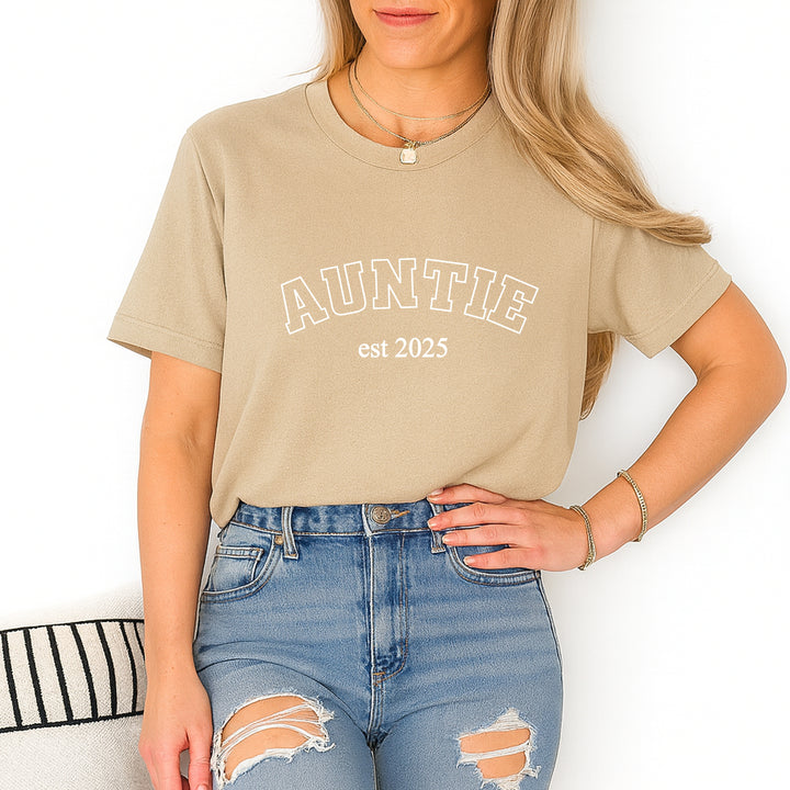 Person wearing a beige t-shirt with 'AUNTIE est 2025' text and ripped jeans on a white background